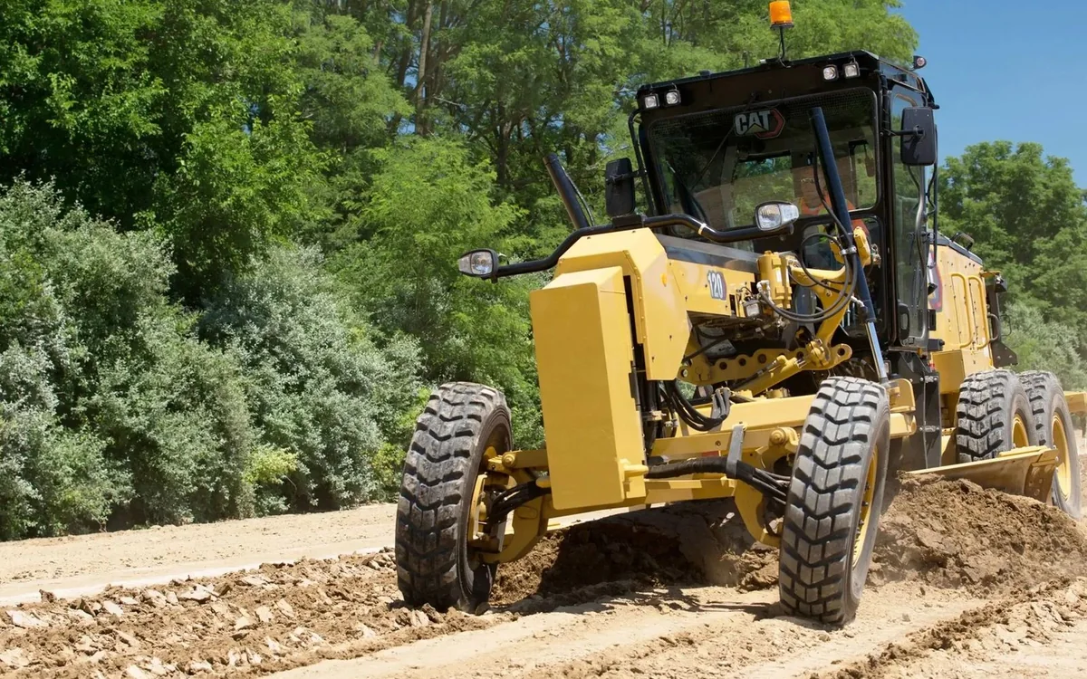 Yellow motor grader preparing an unpaved road surface